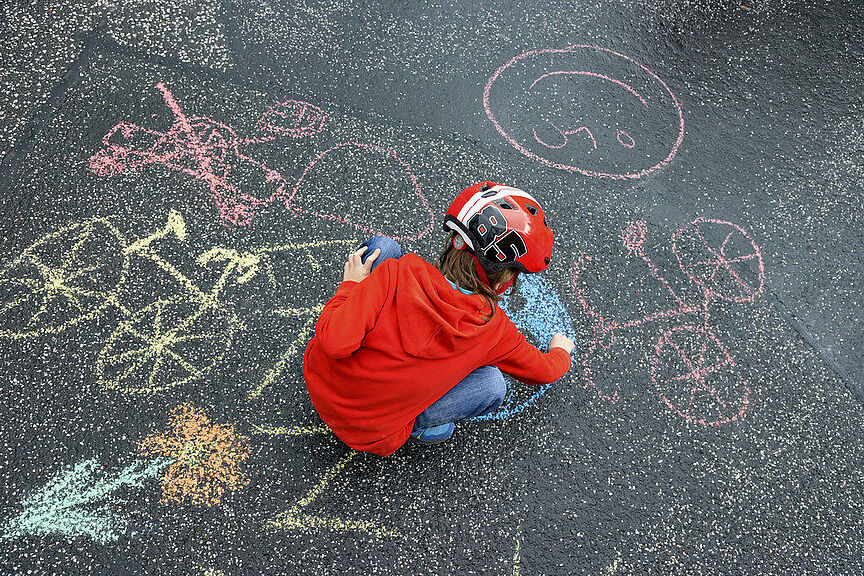 Kind malt mit Kreide Kind hat Fahrradhelm auf und mal mit Kreide auf die Straße bei der Kidical Mess