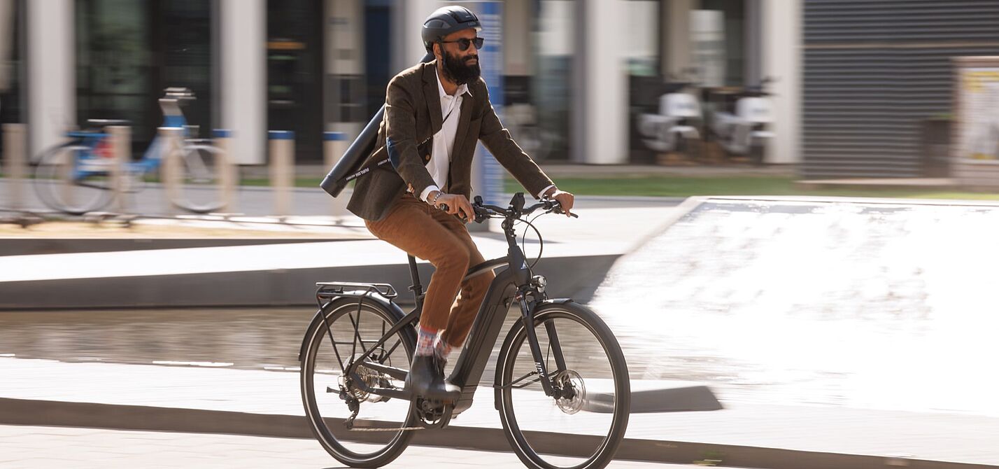 Urbane Mobilität: Geschäftsmann auf einem Elektrofahrrad in der Stadt Ein Pendler fährt auf seinem elektrischen Fahrrad durch das Stadtgebiet.